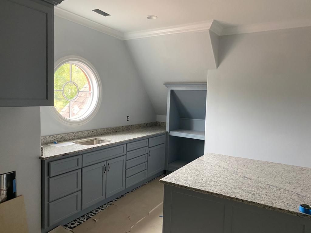 A kitchen with gray cabinets , granite counter tops , and a round window.