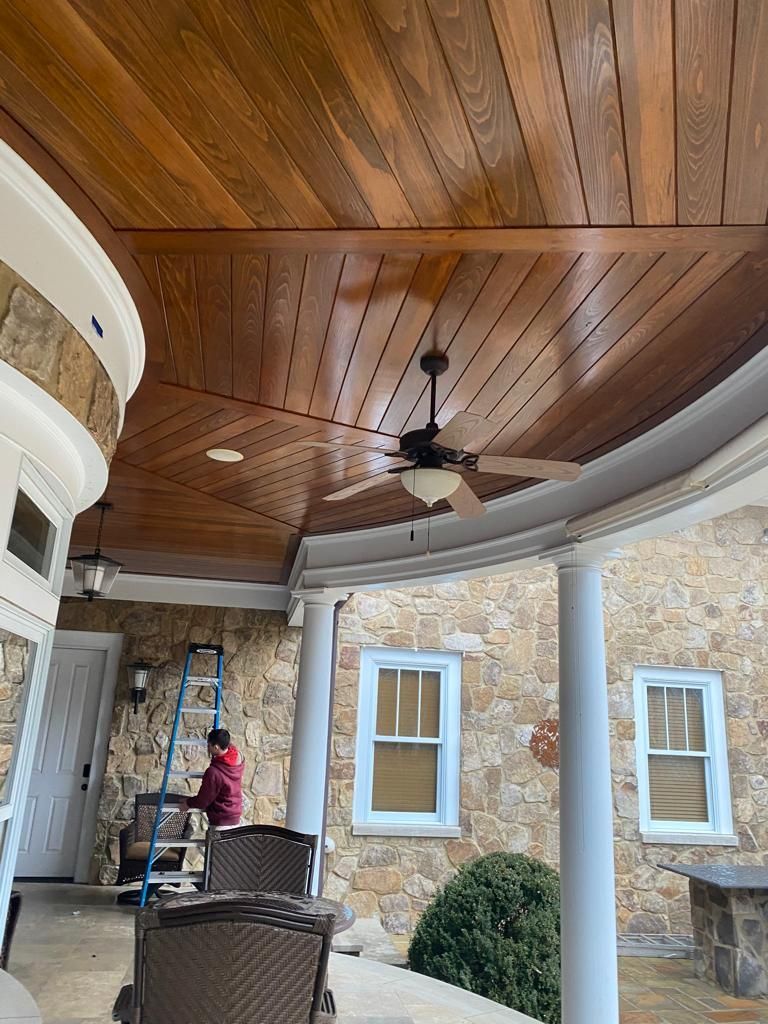 A man is painting the ceiling of a porch with a ceiling fan.
