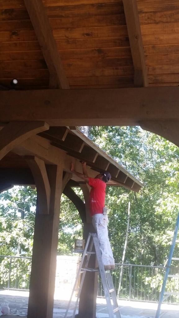 A man is standing on a ladder painting a wooden structure.