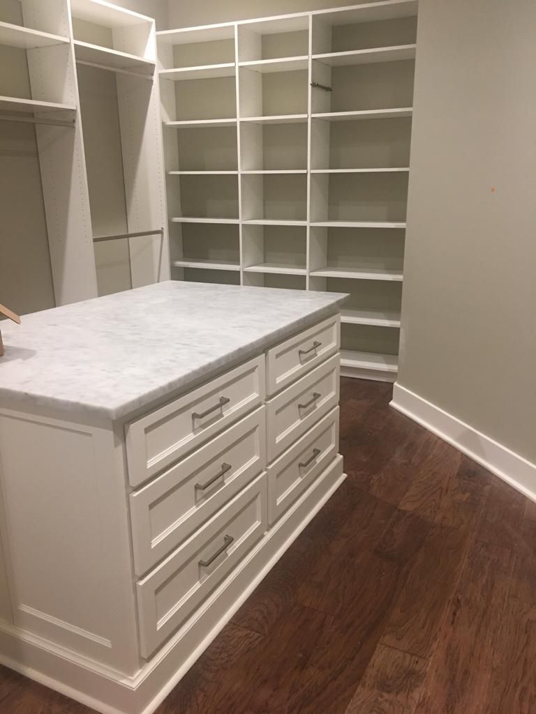 A walk in closet with lots of shelves and drawers and a large island in the middle.