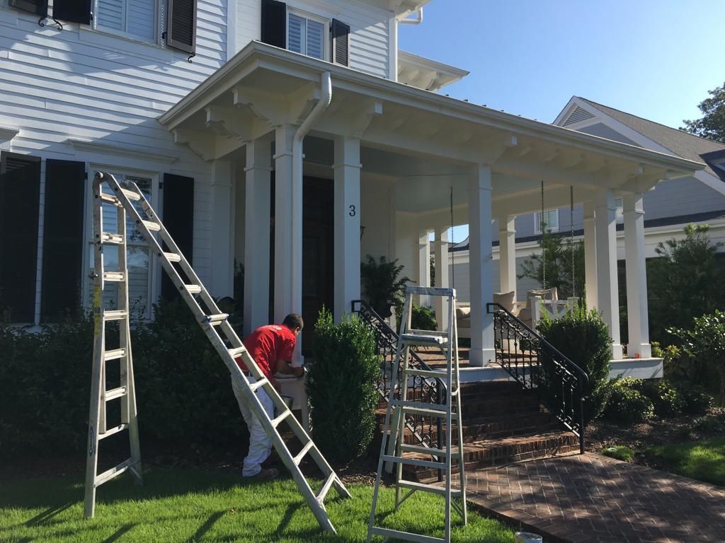 A man is standing on a ladder in front of a white house.