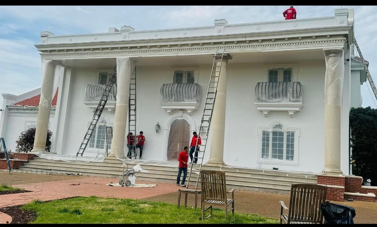A large white house is being painted by a group of people.