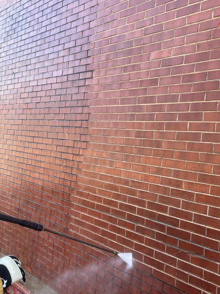 A person is cleaning a brick wall with a high pressure washer.