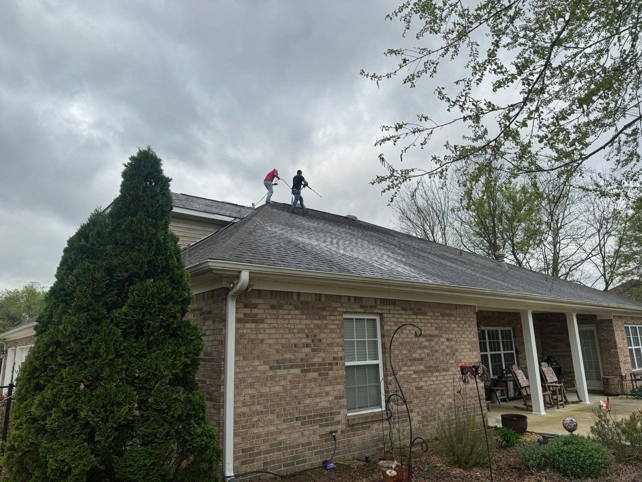 Two men are working on the roof of a brick house.