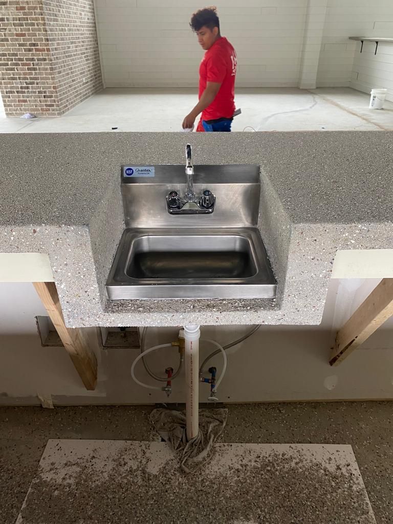 A man in a red shirt is standing next to a sink in a kitchen.