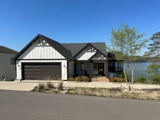 A large white and black house with a garage next to a lake.