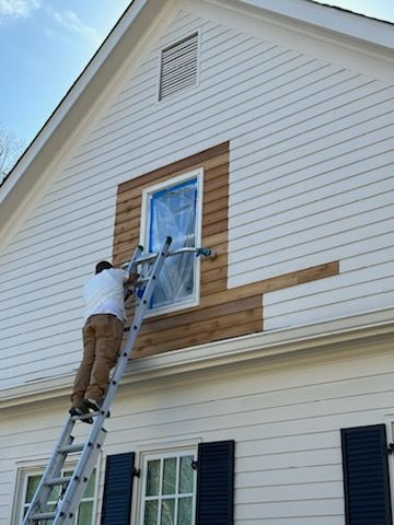 A man is standing on a ladder painting the side of a house.