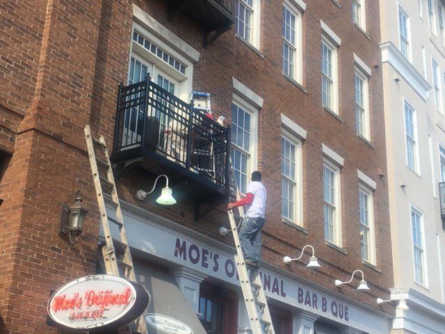 A man is standing on a ladder in front of a building that says moe 's original barbecue