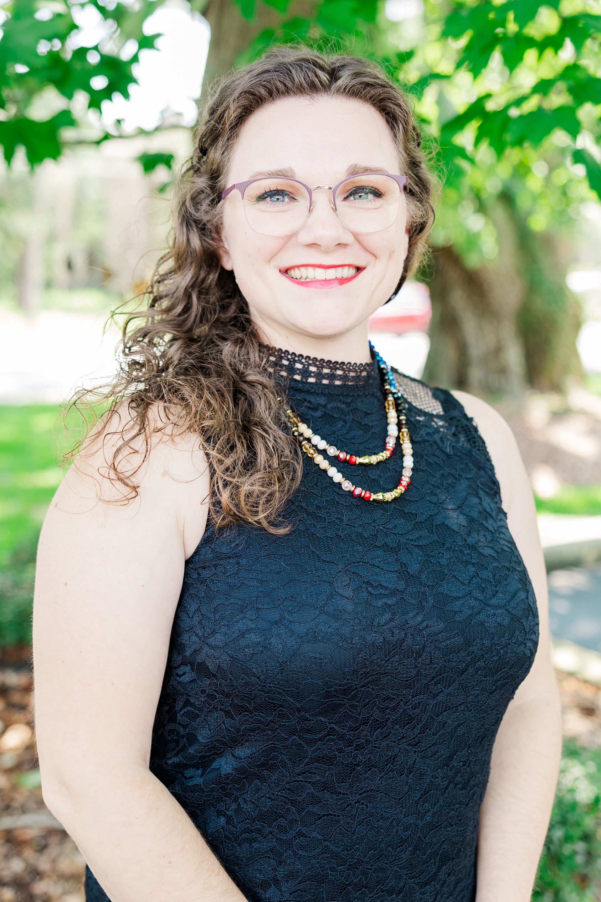 A woman in a black dress and glasses is smiling for the camera.