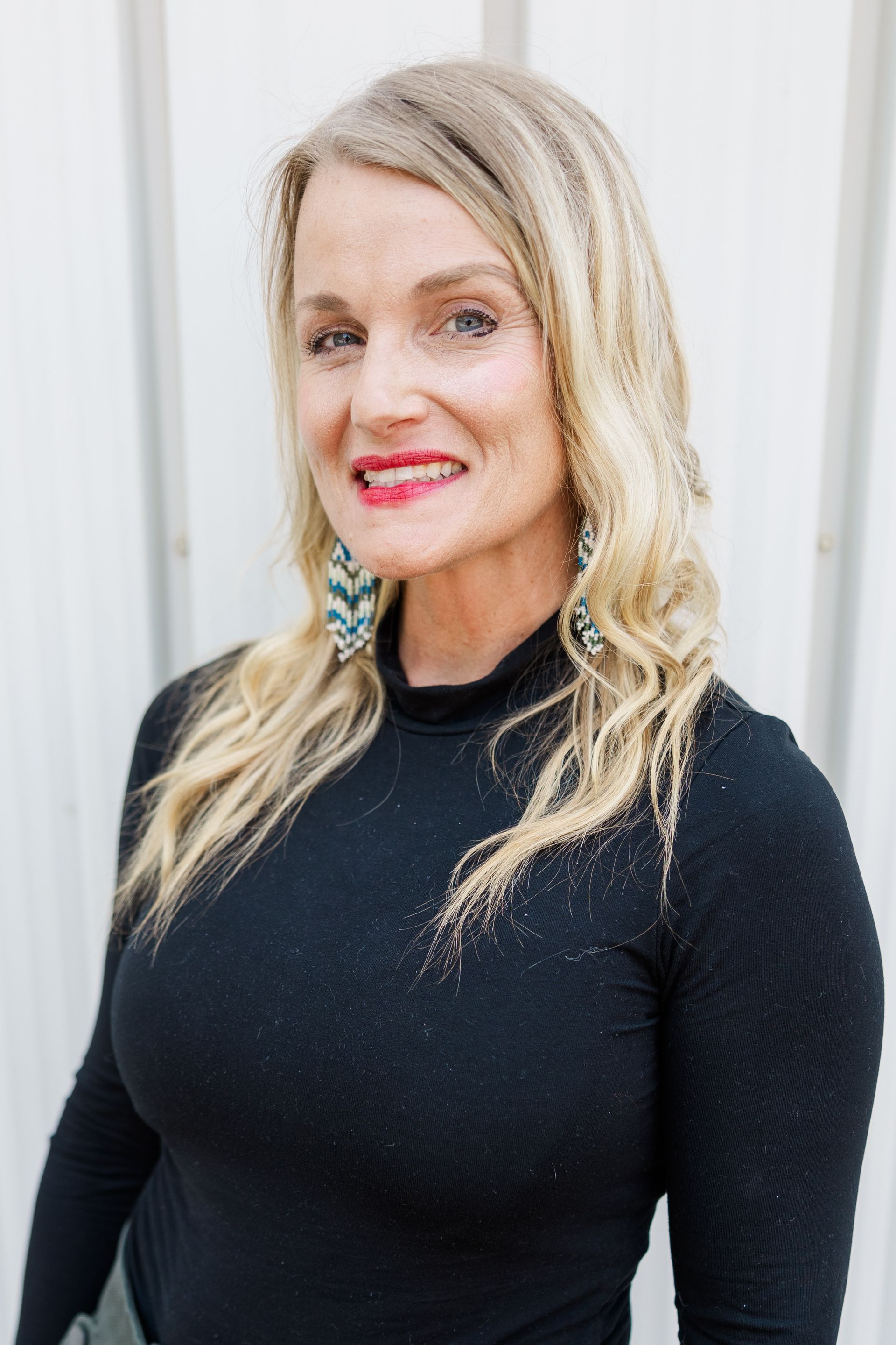 A woman wearing a black sweater and earrings is smiling for the camera.