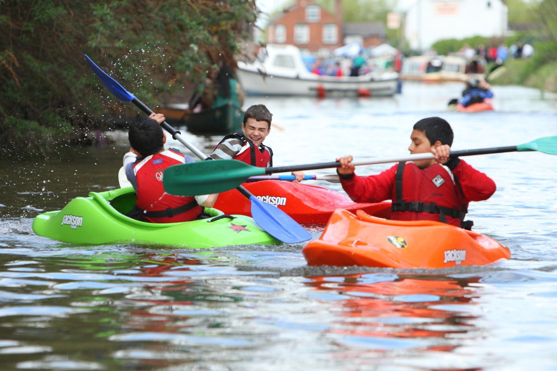 Mae grŵp o bobl yn padlo caiacau ar afon.