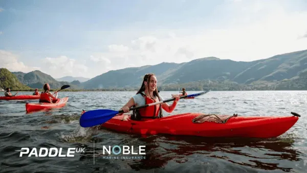 A woman is paddling a red kayak on a lake.