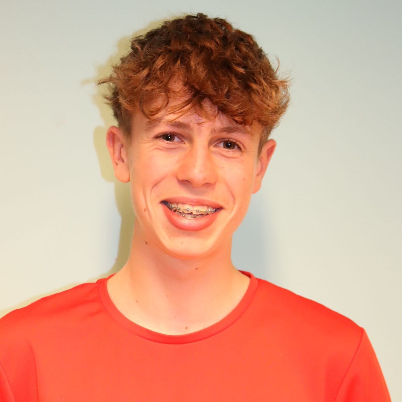 A young man with braces on his teeth is wearing a red shirt