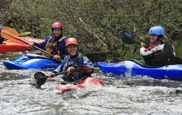 Mae grŵp o bobl yn reidio caiacau i lawr afon.