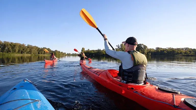 A man is paddling a red kayak on a lake.