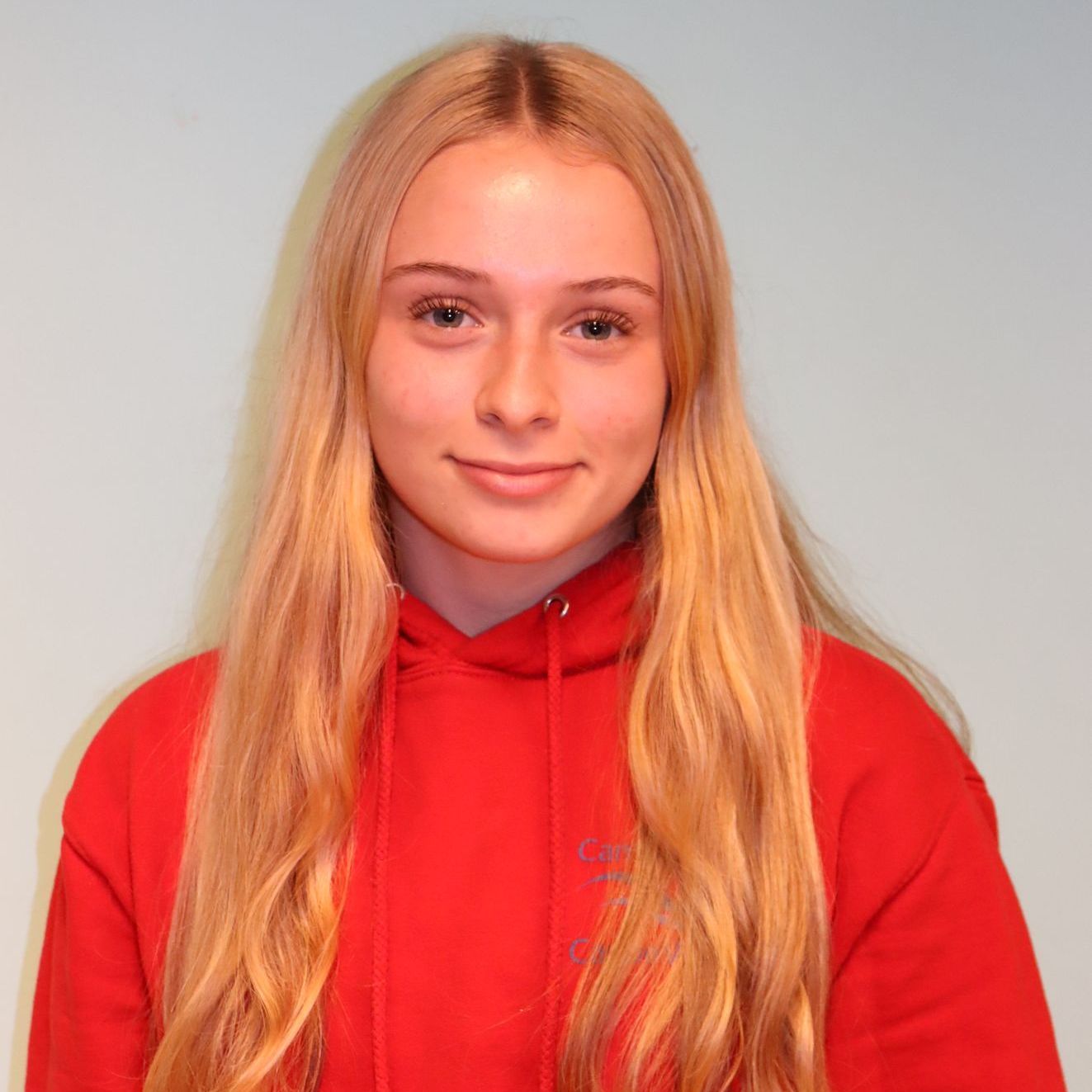 A young woman with long blonde hair is wearing a red hoodie.
