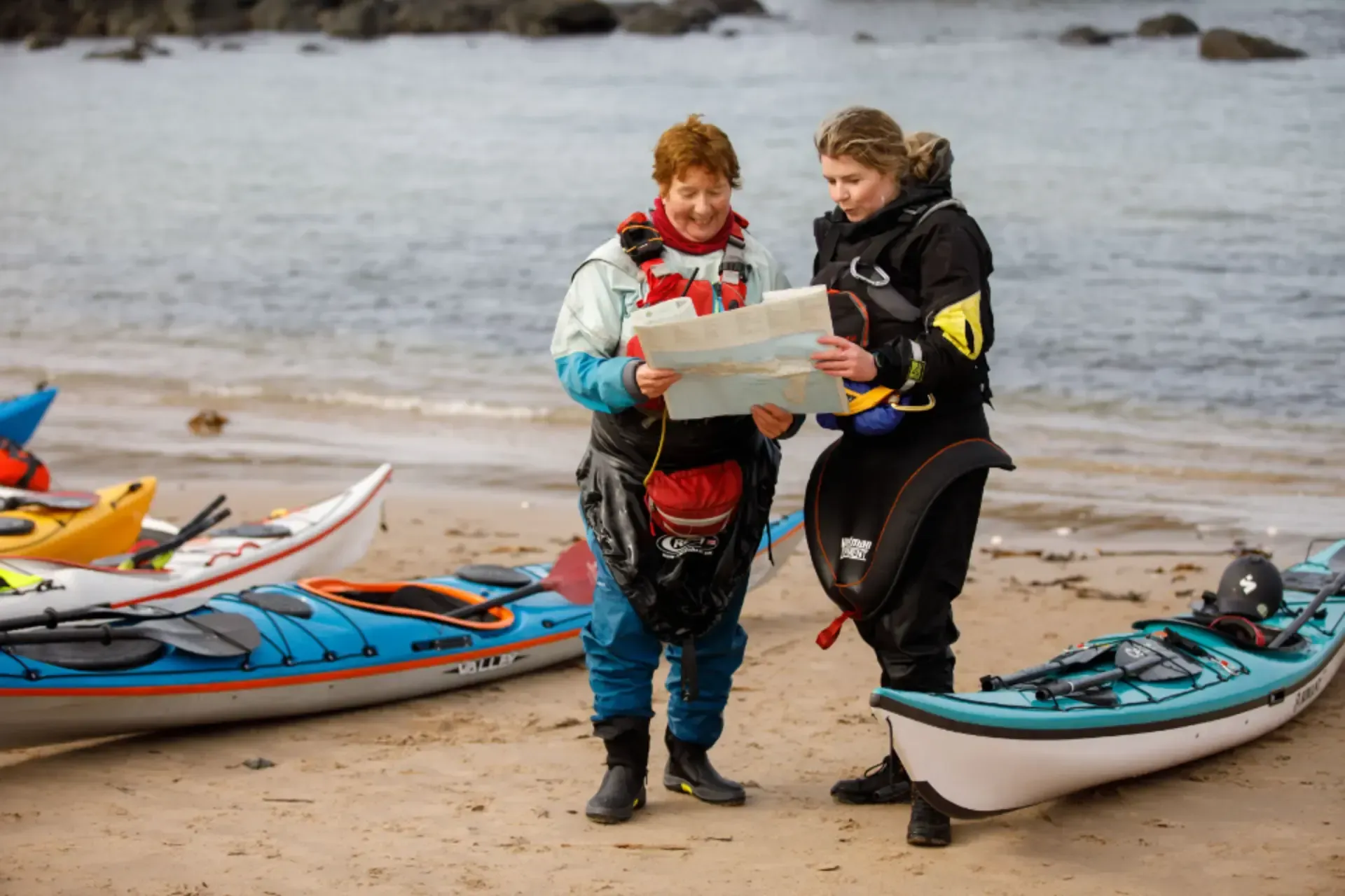 Dwy fenyw yn sefyll ar draeth yn edrych ar fap.