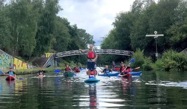 Mae grŵp o bobl yn reidio caiacau i lawr afon.