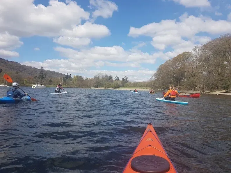 Mae grŵp o bobl yn rhwyfo caiacau ar lyn.