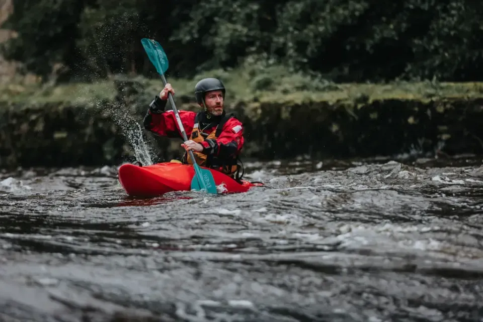 A man is paddling a red kayak down a river.