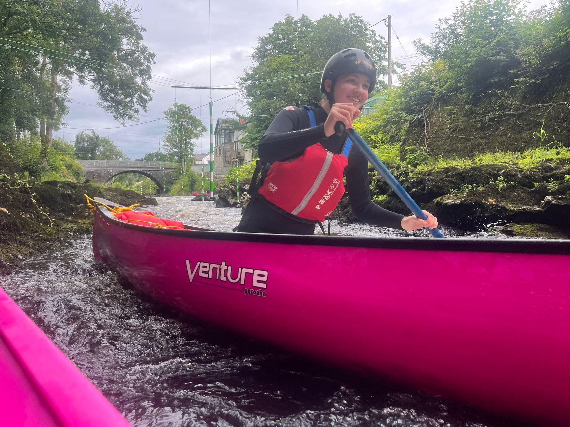 A woman is paddling a pink canoe through a river.