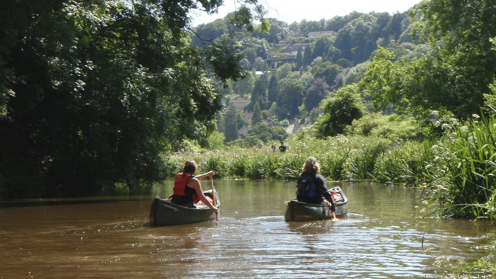 Two people in canoes are paddling down a river