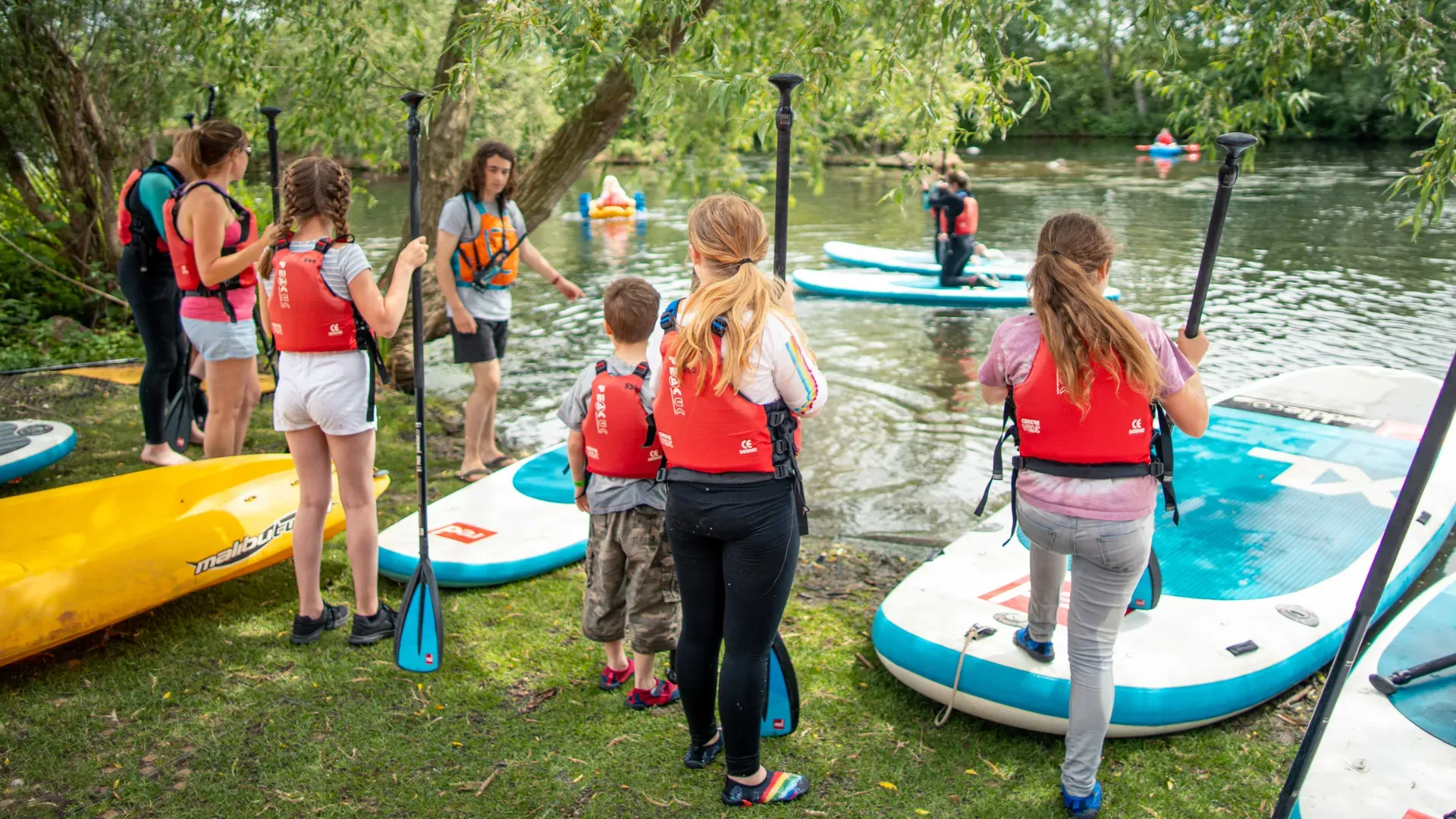 A group of people are standing next to a body of water holding paddle boards.