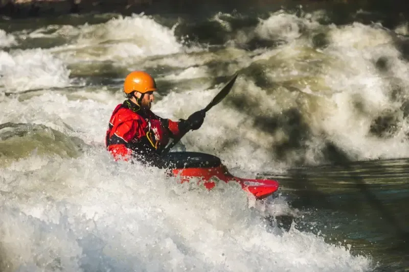 A man is riding a kayak down a river.