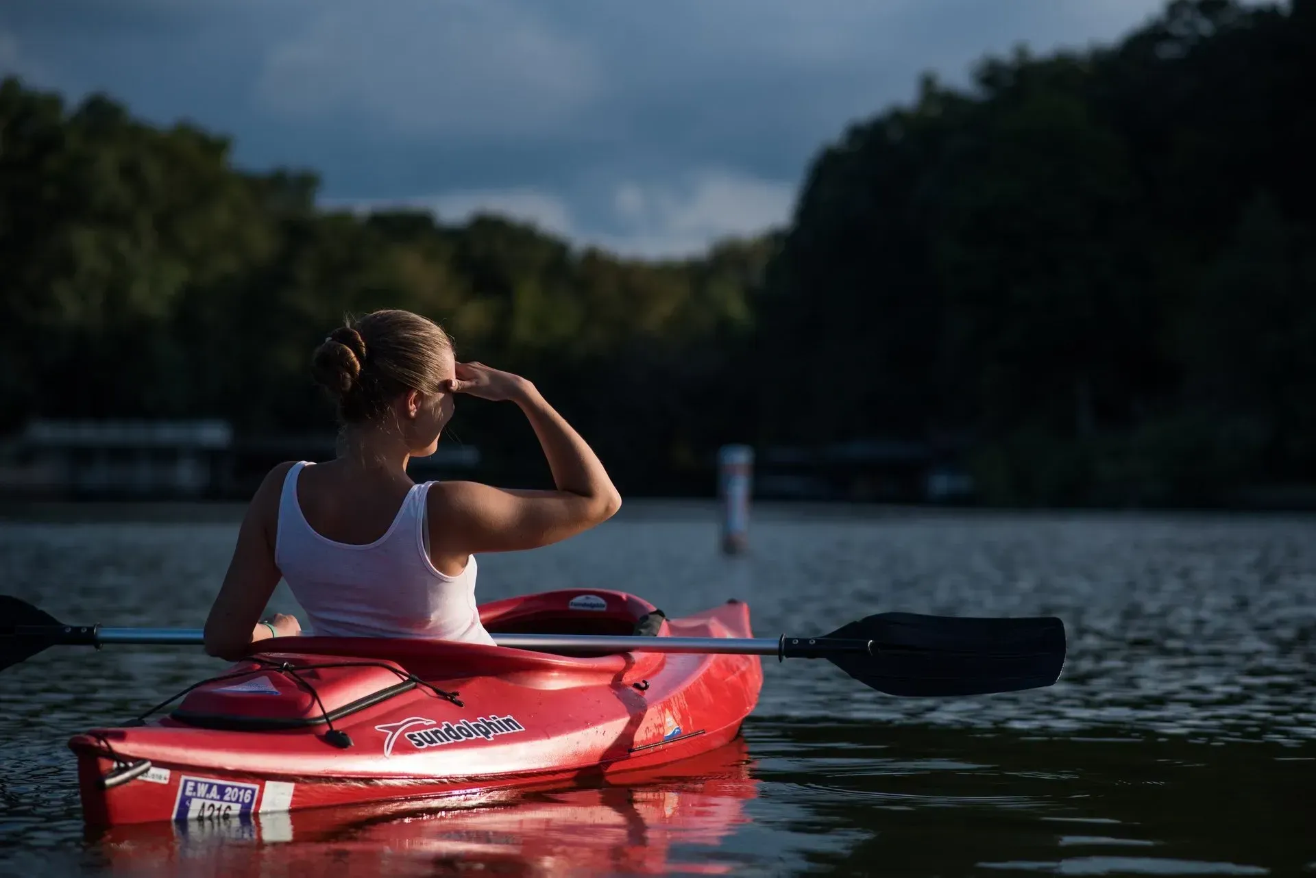 A woman is sitting in a red kayak on a lake.