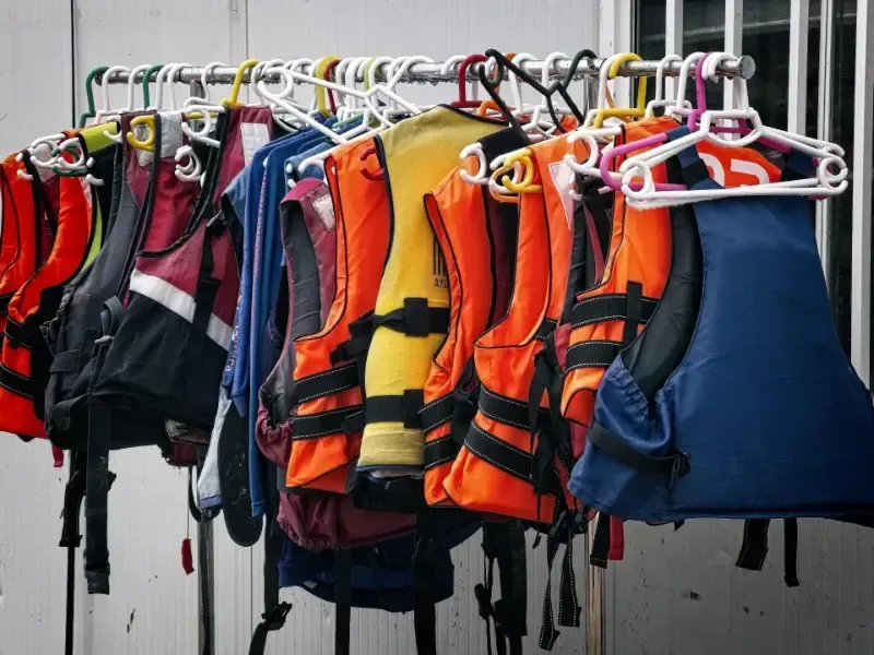 A bunch of life jackets are hanging on a rack.