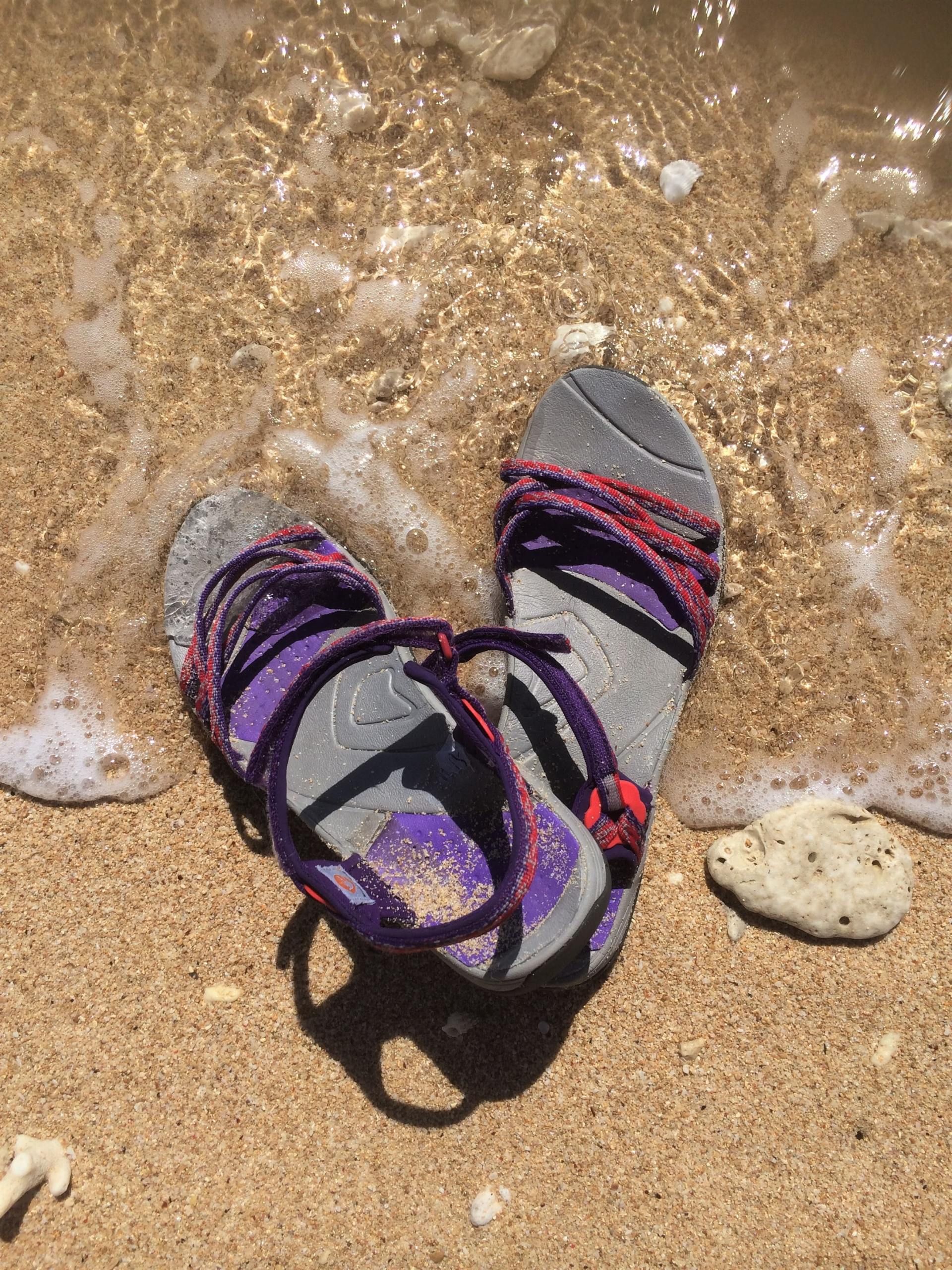 A pair of sandals are laying on the sand on the beach.
