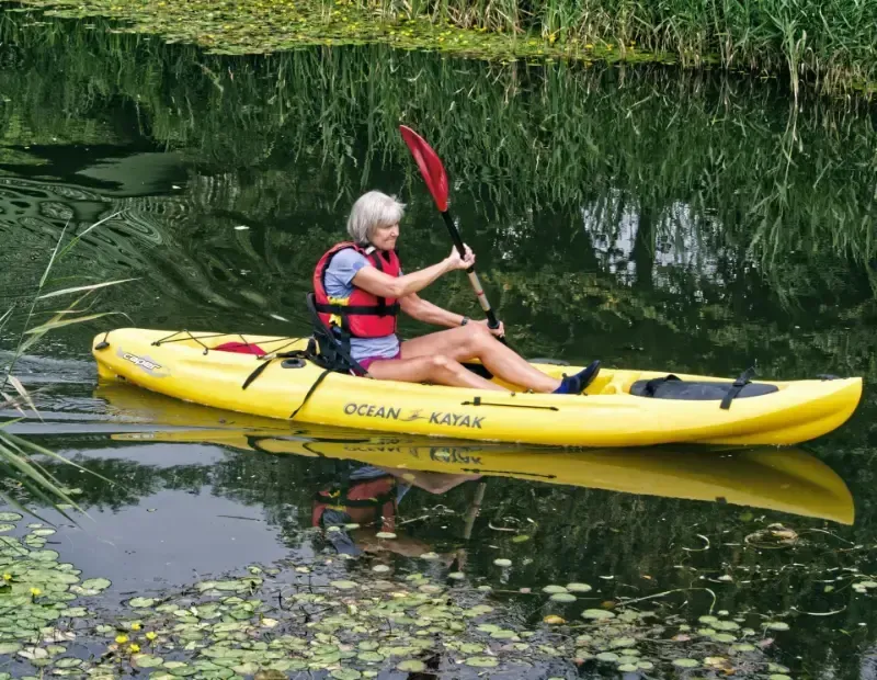 A woman is paddling a yellow ocean kayak