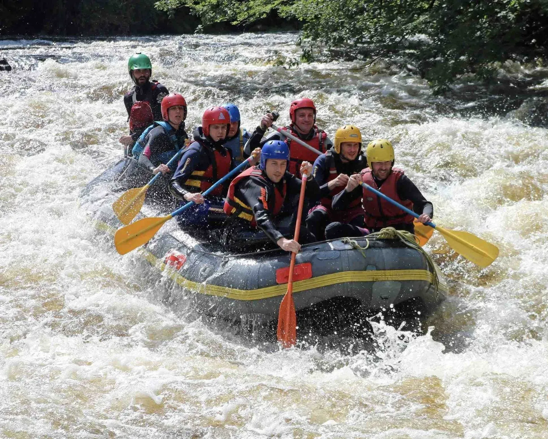 Mae grŵp o bobl yn rafftio i lawr afon mewn rafft.