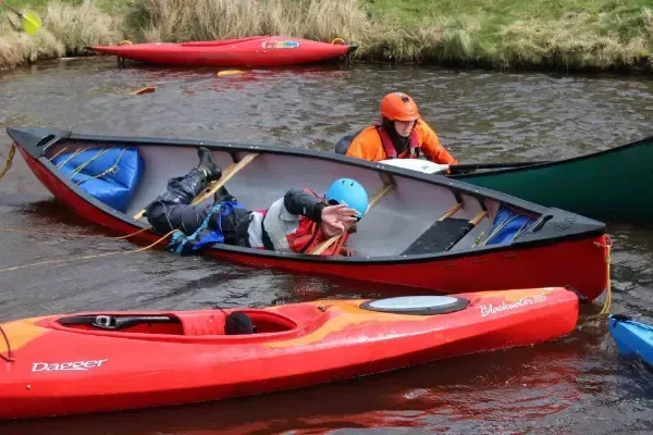 Mae grŵp o bobl yn rhwyfo caiacau ar afon.