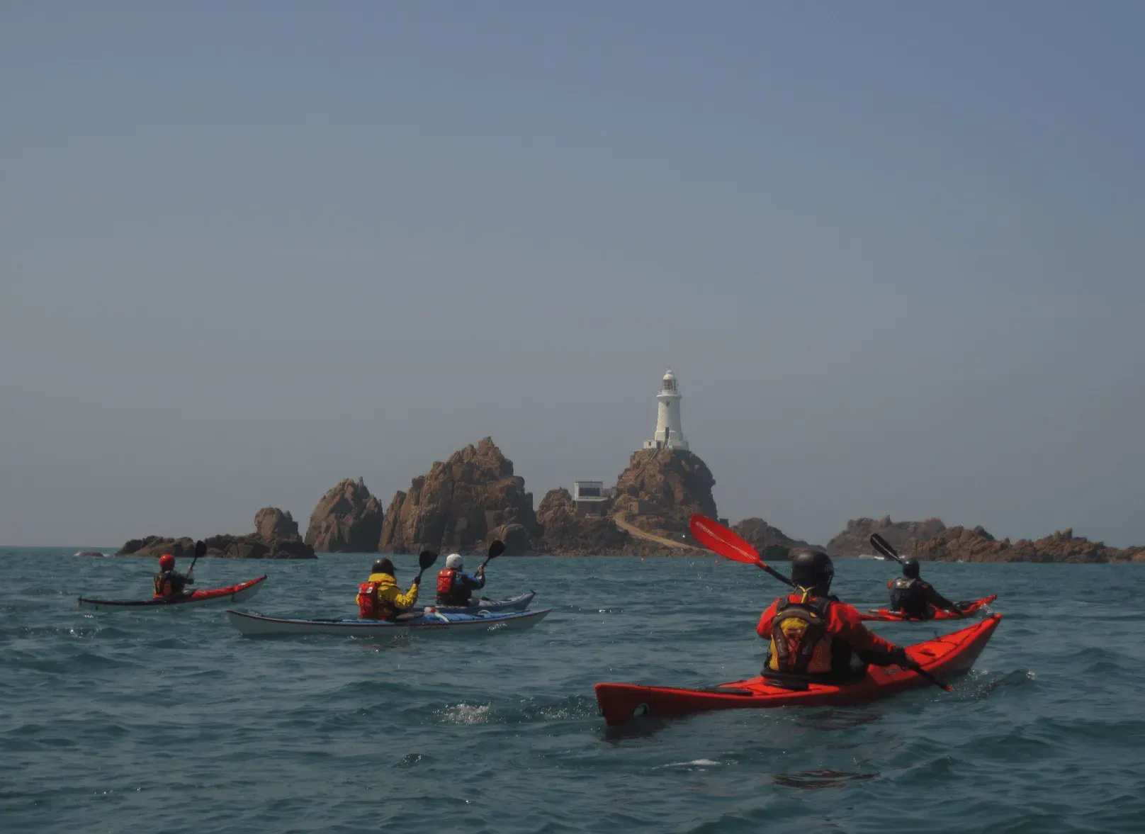 Mae grŵp o bobl yn caiacio yn y môr ger goleudy.