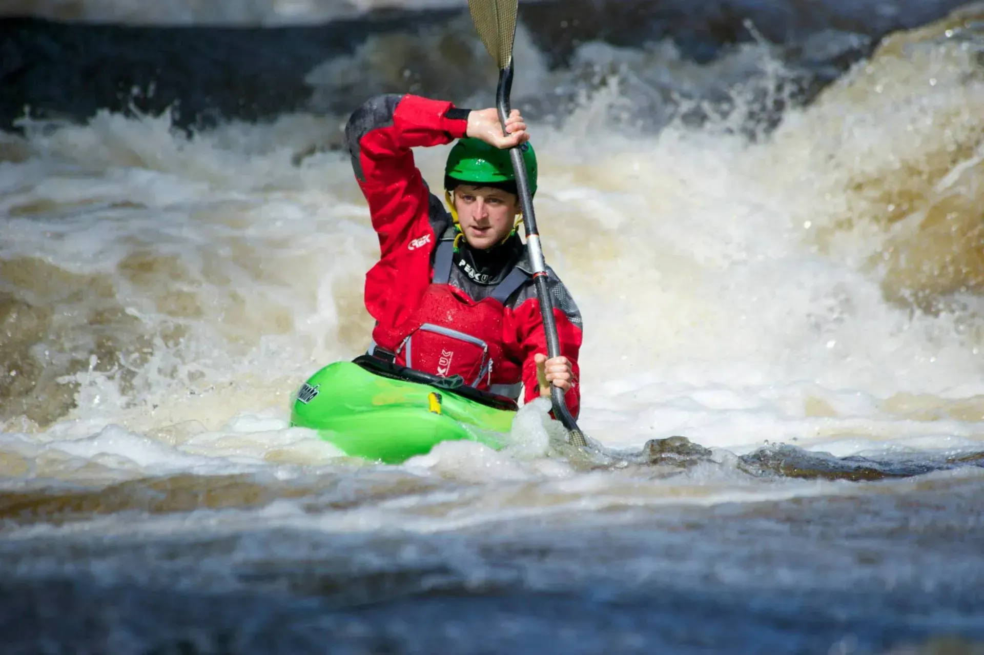 A man in a green kayak is paddling down a river.