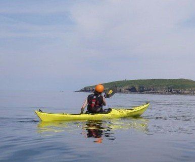 Mae person yn padlo caiac melyn yn y cefnfor.