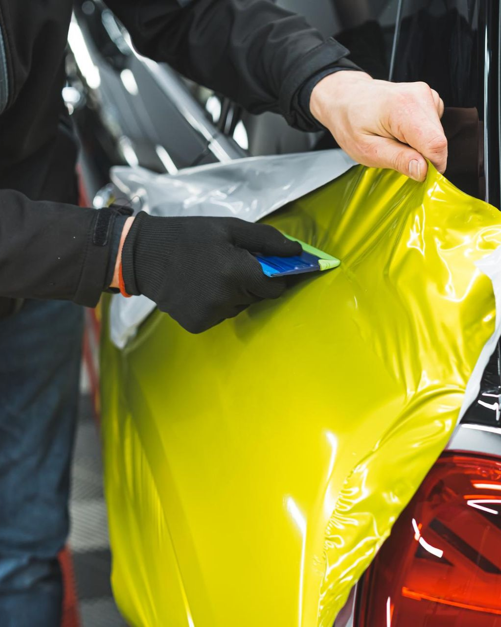 A person wearing black gloves is polishing a black car