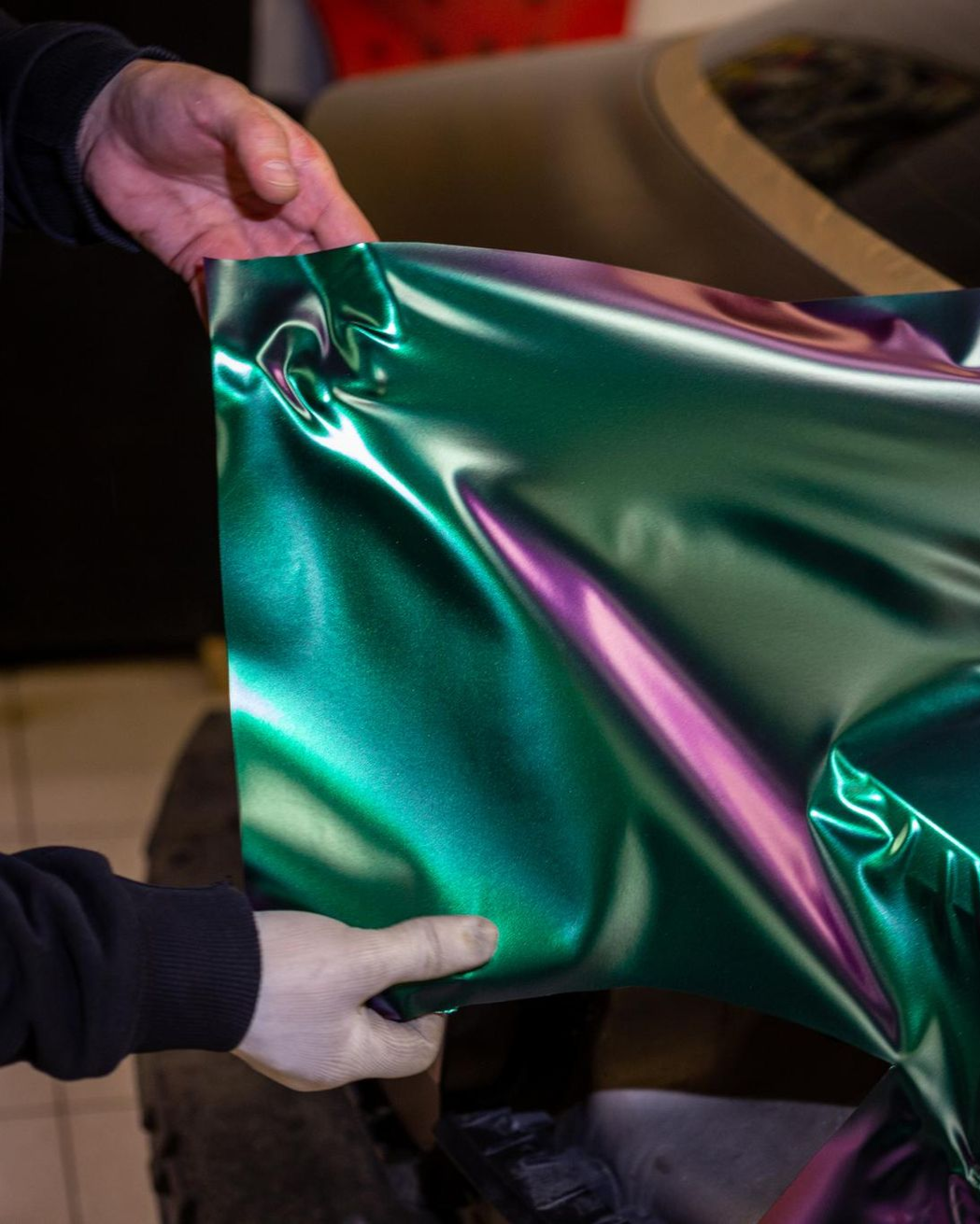 A person wearing black gloves is polishing a black car