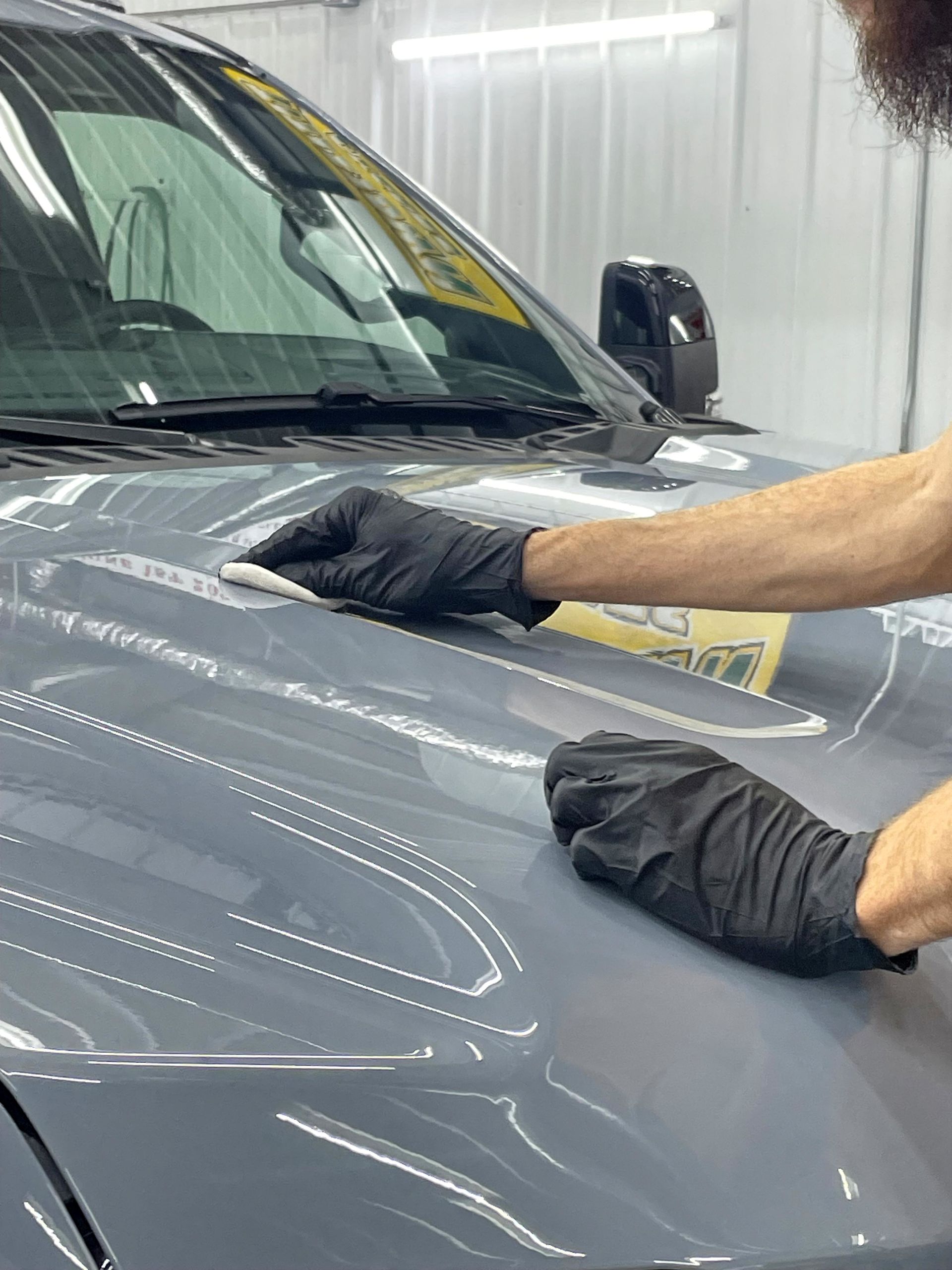 A person is polishing the hood of a blue car.