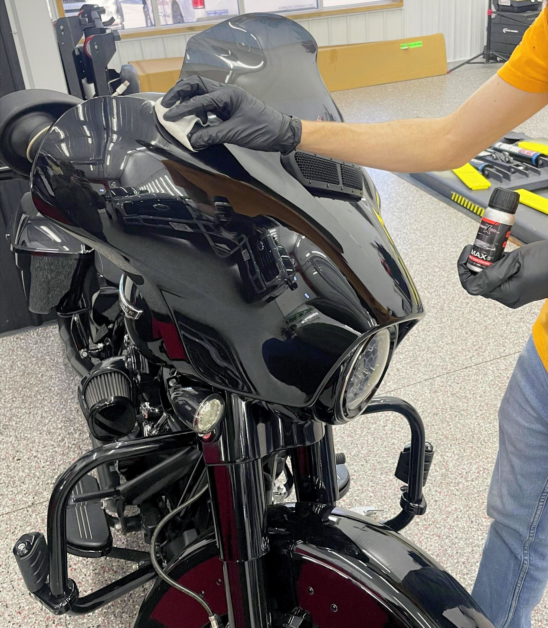 A person wearing black gloves is polishing a black car