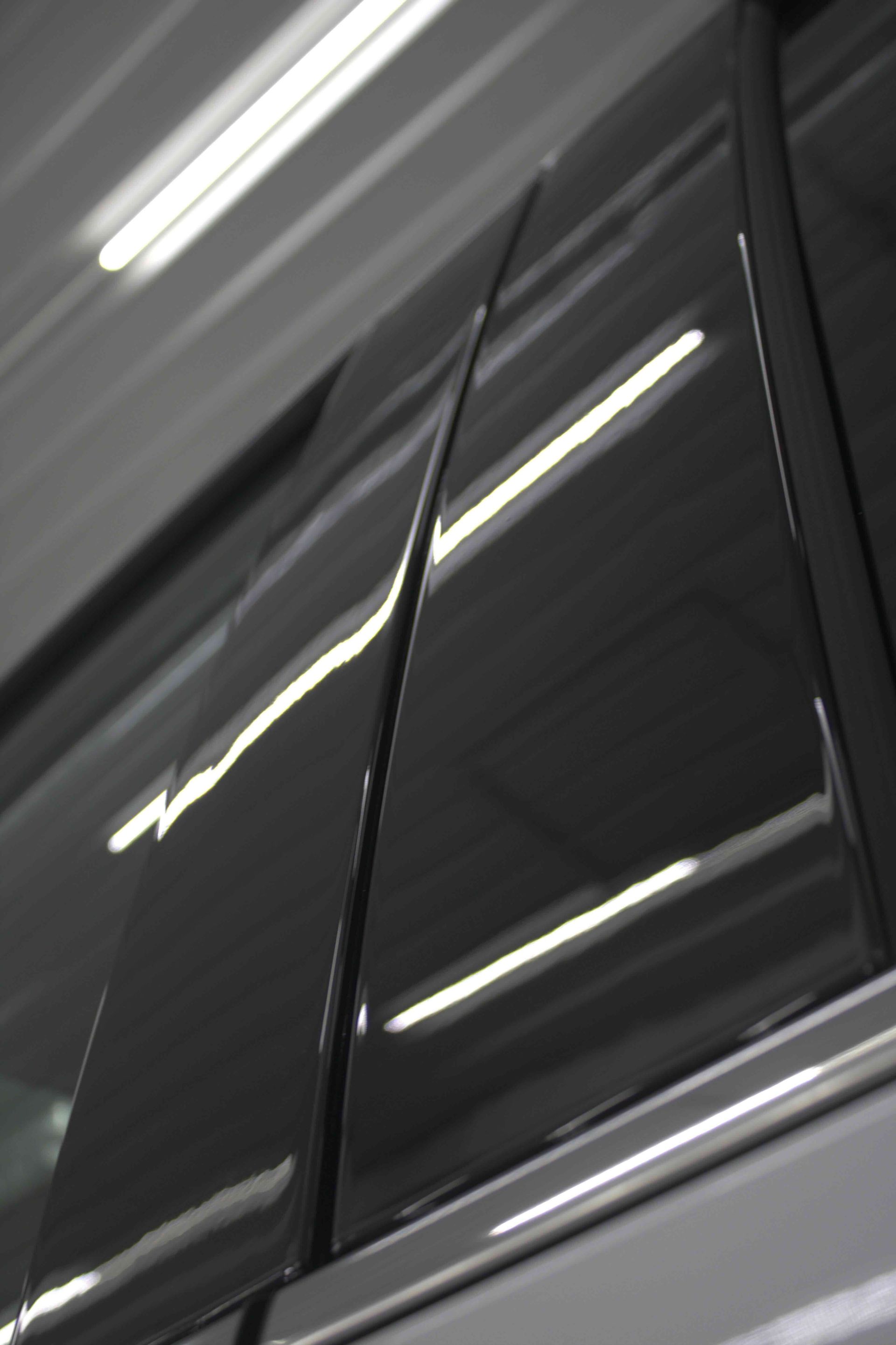 A person wearing black gloves is polishing a black car