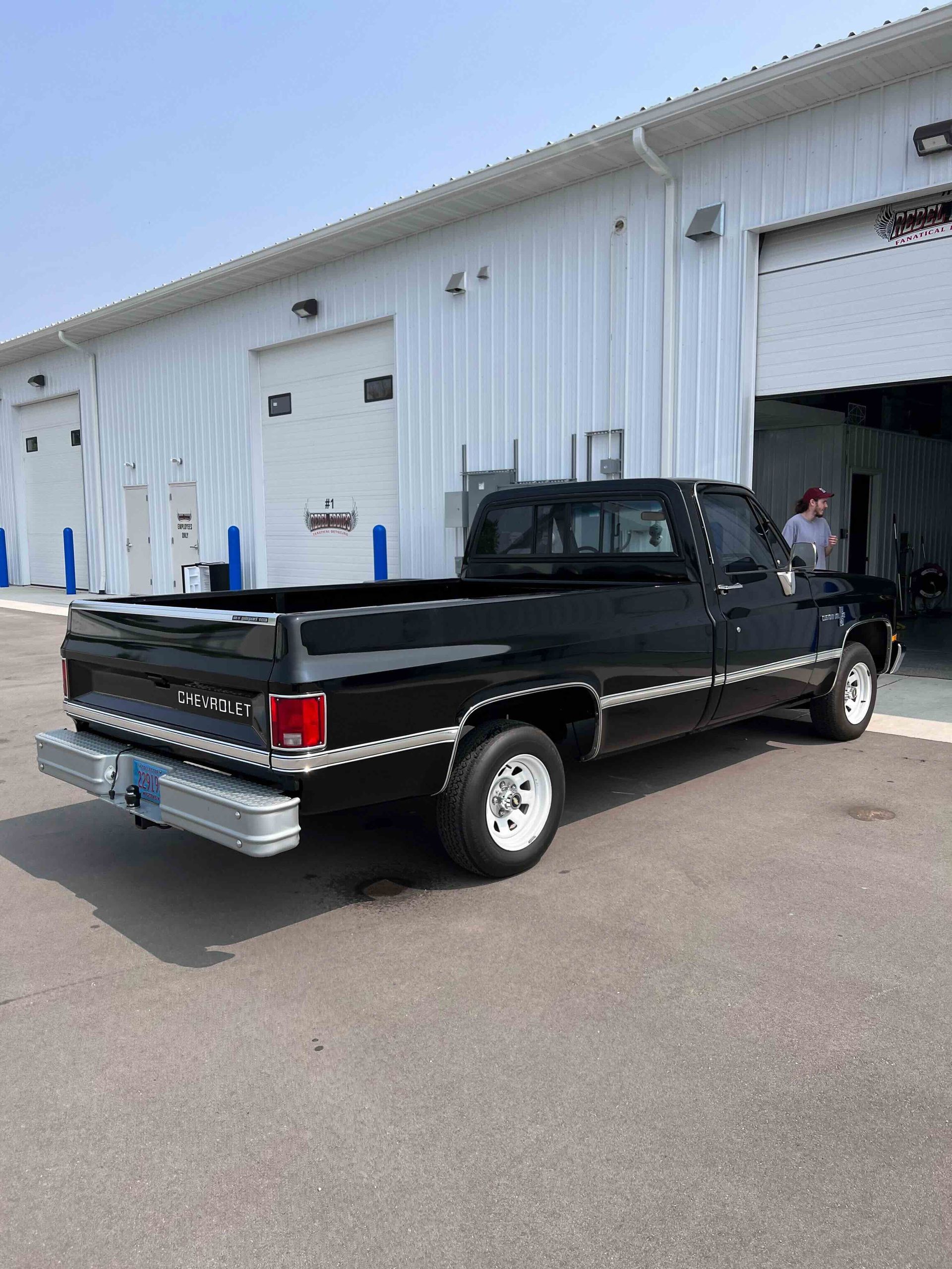 A man is cleaning the wheel of a black car with a sponge.