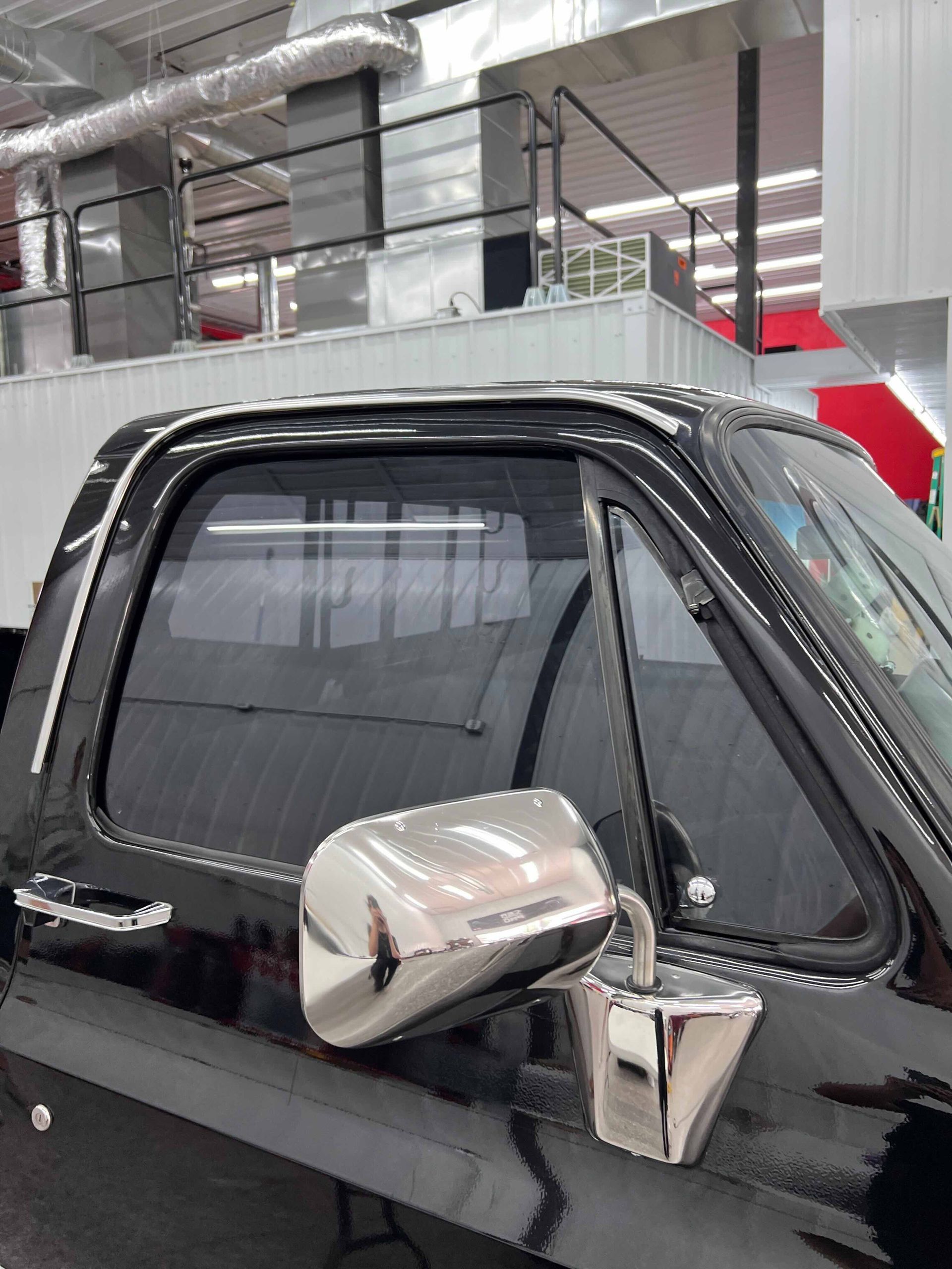 Black pickup truck with tinted windows and chrome side mirror in a shop.