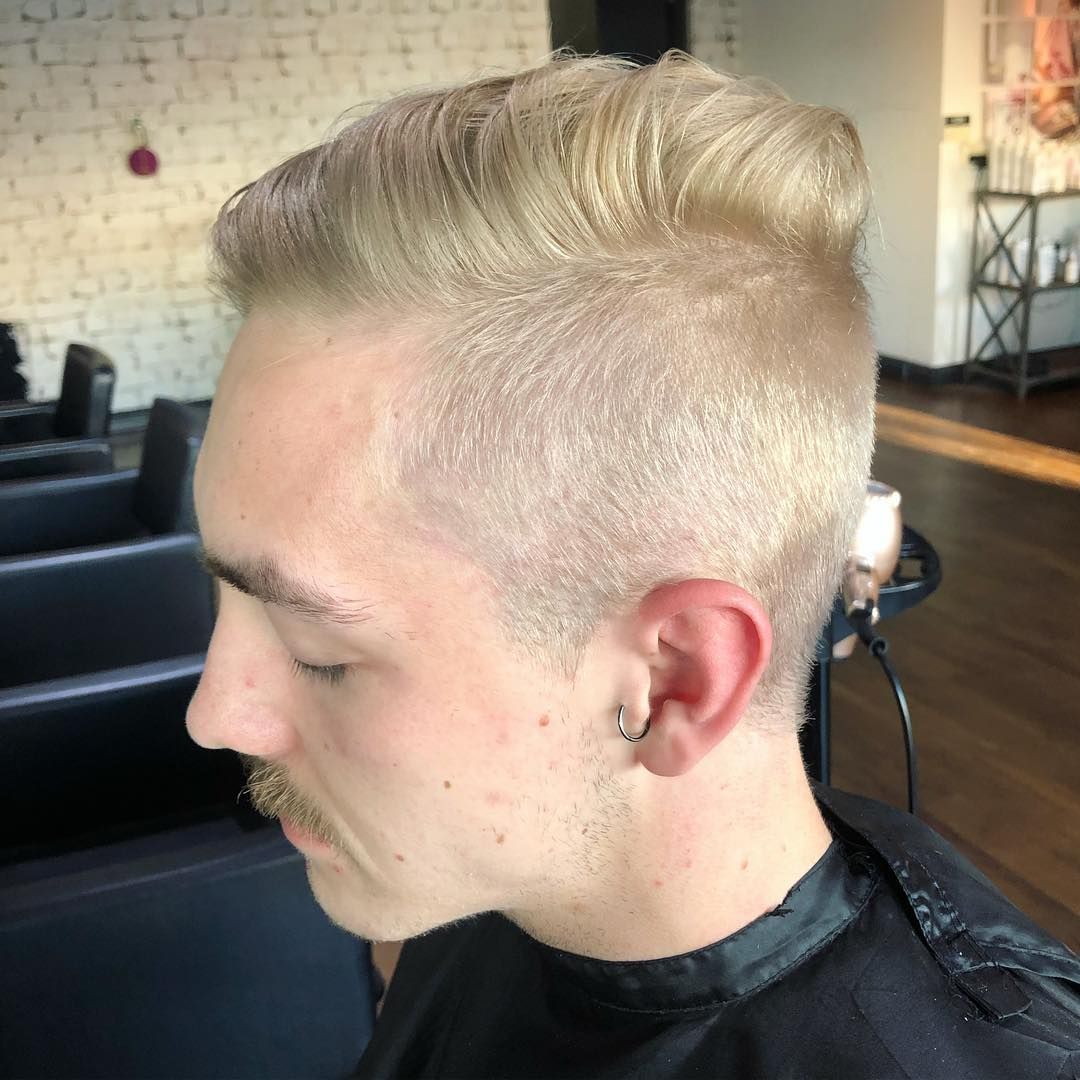 Blond-haired person with a styled pompadour hairstyle and mustache, indoors at a salon.