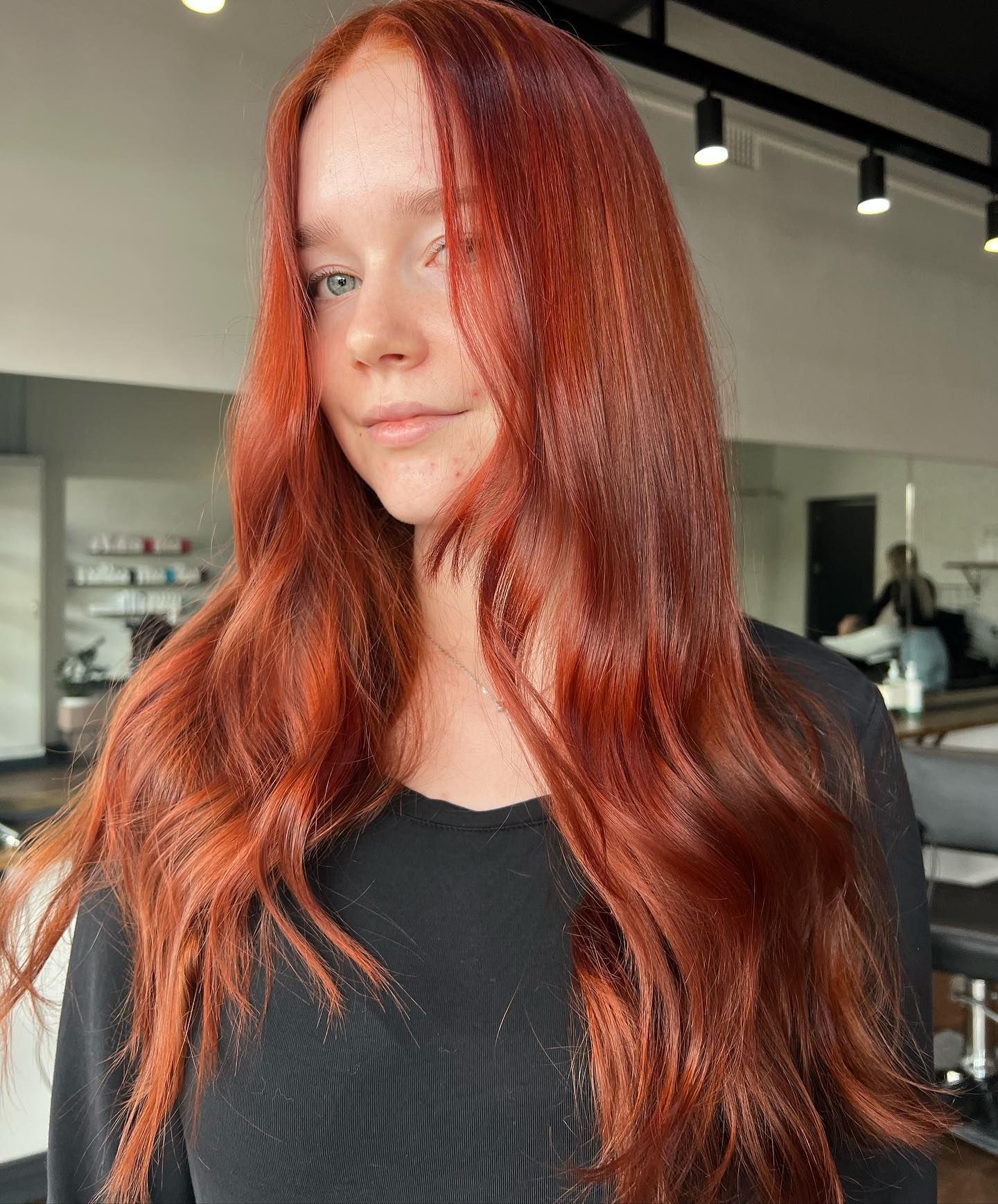 Woman with long, wavy red hair in a salon, wearing a black top.