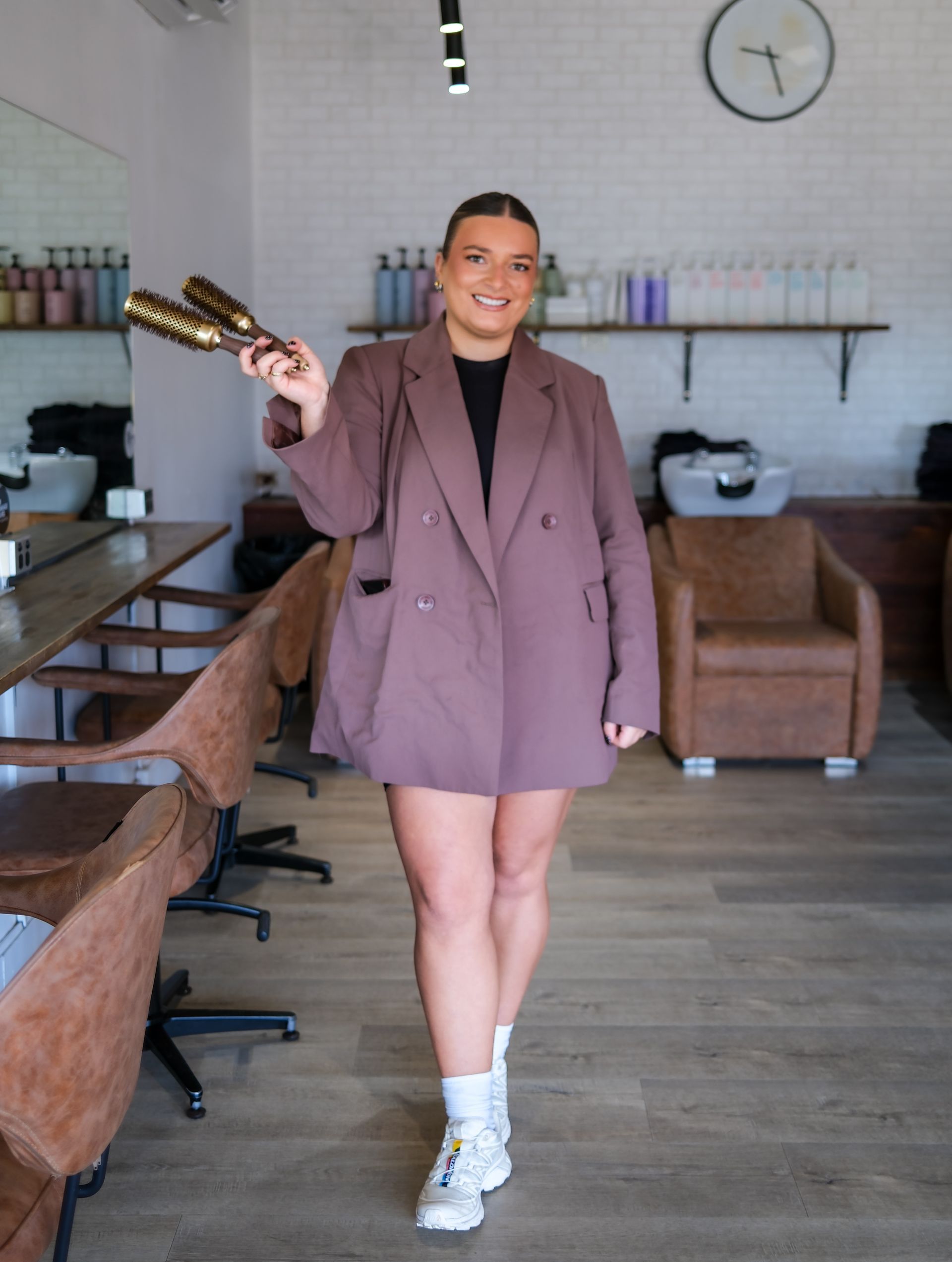 Woman in a blazer holds hair styling brushes in a salon.
