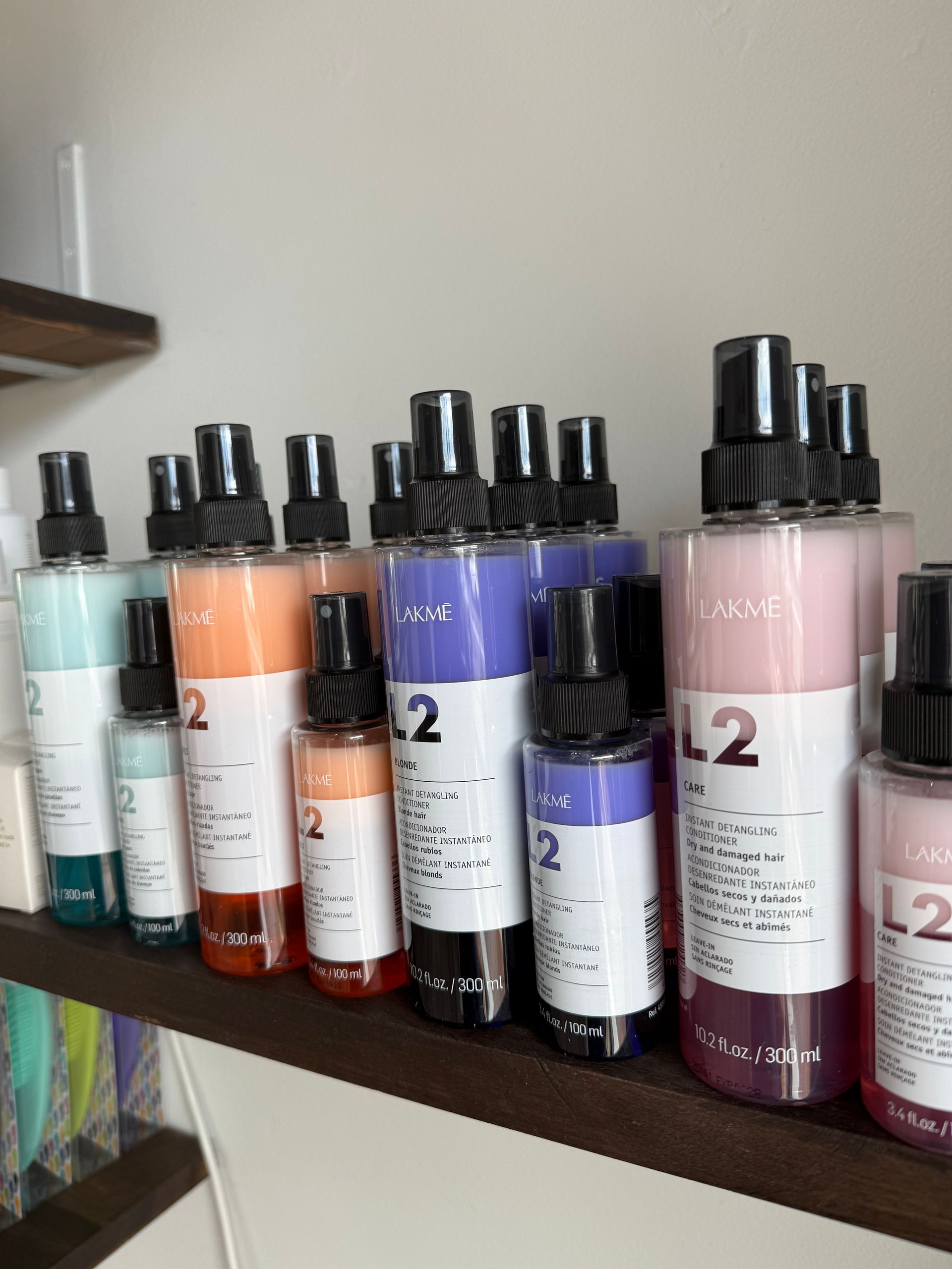 Row of pastel-colored shampoo bottles with black pumps on a wooden shelf against a white brick wall.