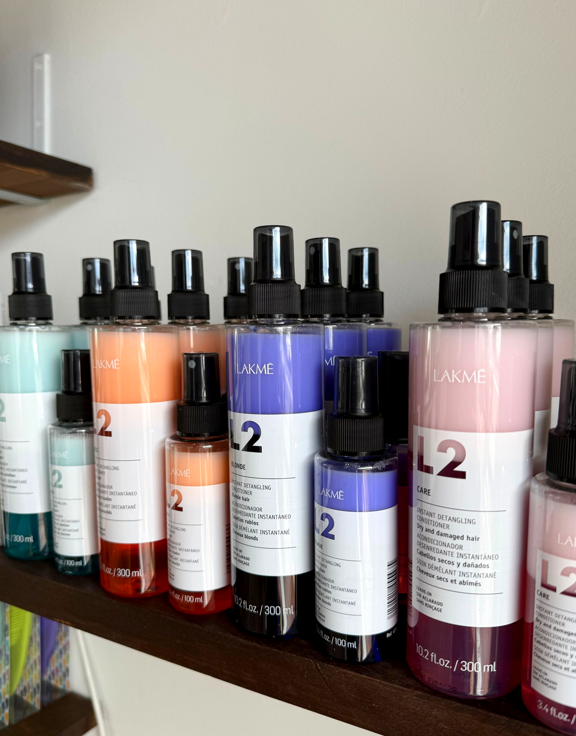 Shelf of various colored L2 brand spray bottles with black tops.