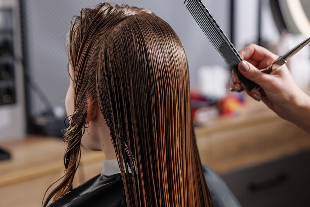 Hairdresser cutting wet hair with scissors and comb in a salon.